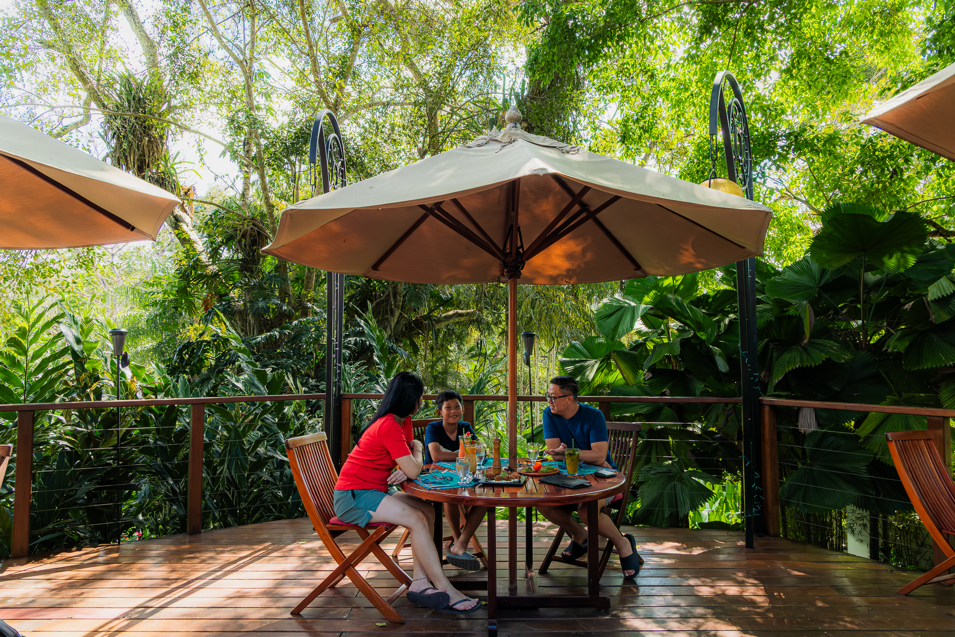 Family enjoying a meal together on the bar patio at The Lodge at Chaa Creek in Belize, surrounded by tropical greenery.
